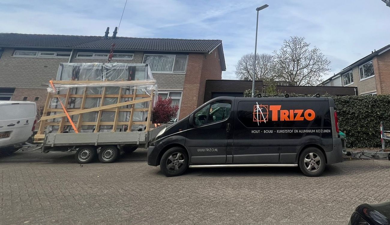 Bedrijfsbus van Trizo met een aanhanger vol ingepakte kozijnen, klaar voor plaatsing bij een woning