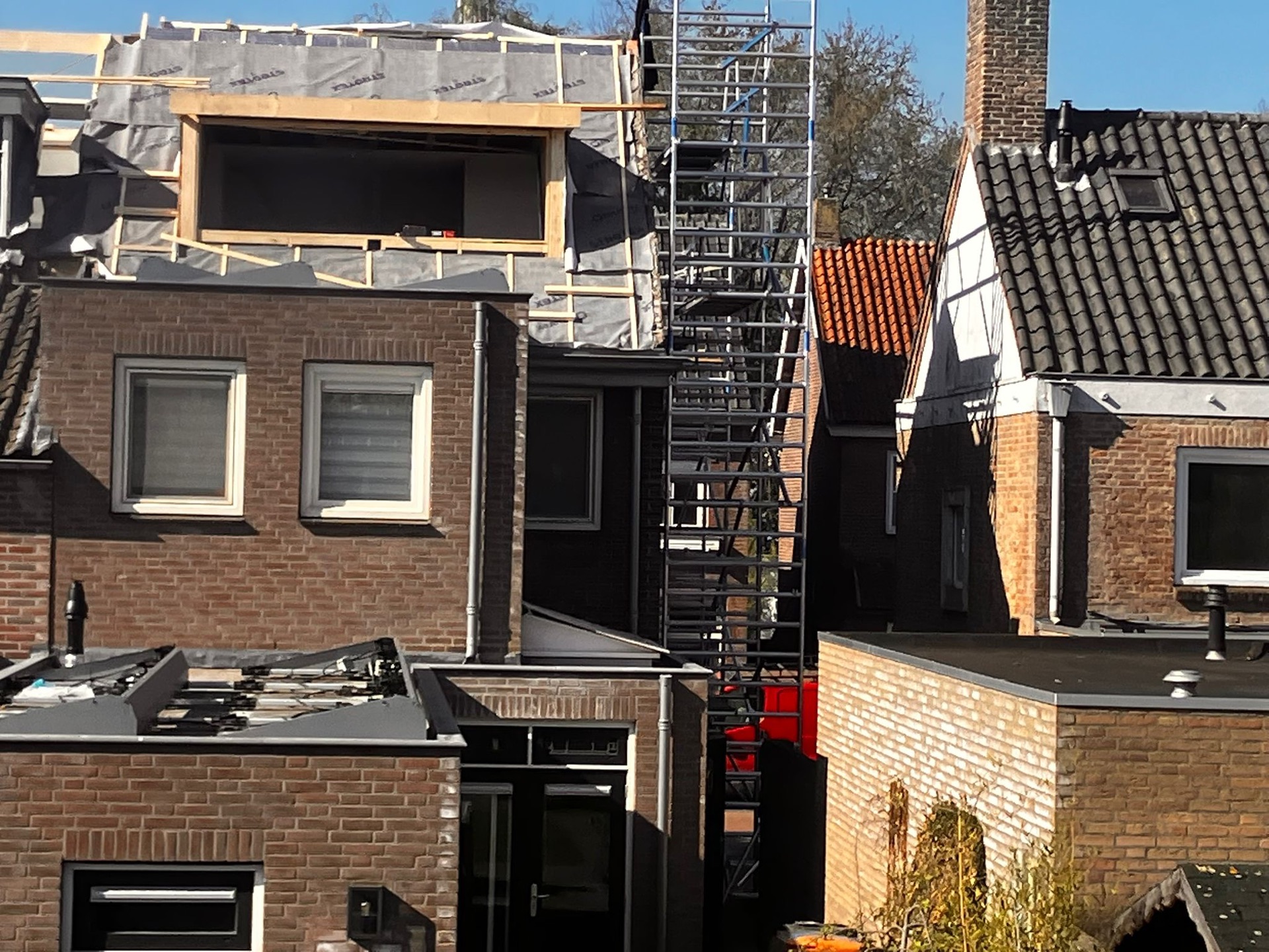 Nieuwe dakopbouw met kozijnopening in aanbouw, met steiger en hoogwerker tussen de daken