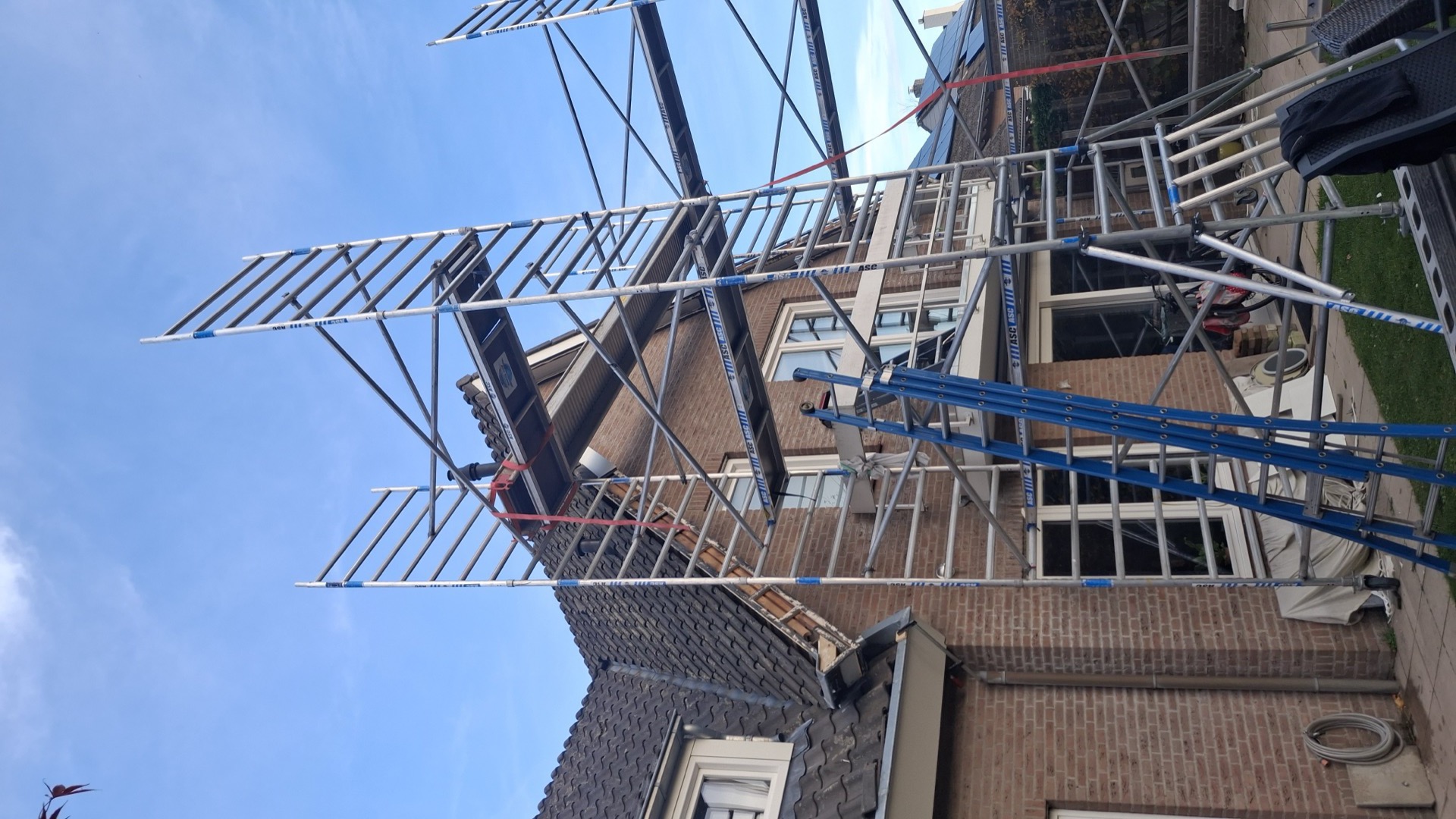 Steigerconstructie rondom een woning, opgebouwd voor dakwerkzaamheden op hoogte