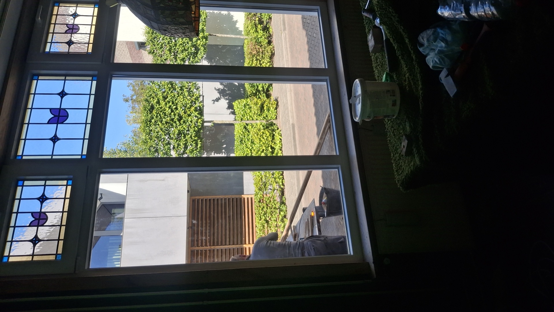 Sierlijk kozijn met glas-in-lood bovenlichten vanuit de woonkamer, buiten werkt een vakman aan de gevel