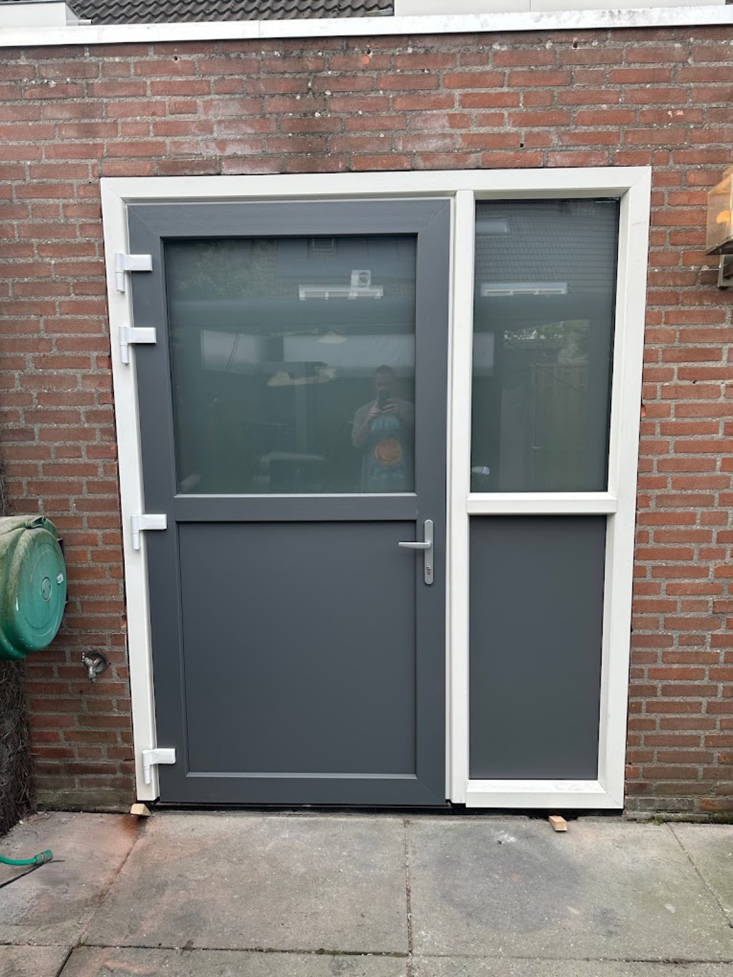Nieuw geplaatste antracietkleurige kunststof achterdeur met glasstrook in een bakstenen gevel