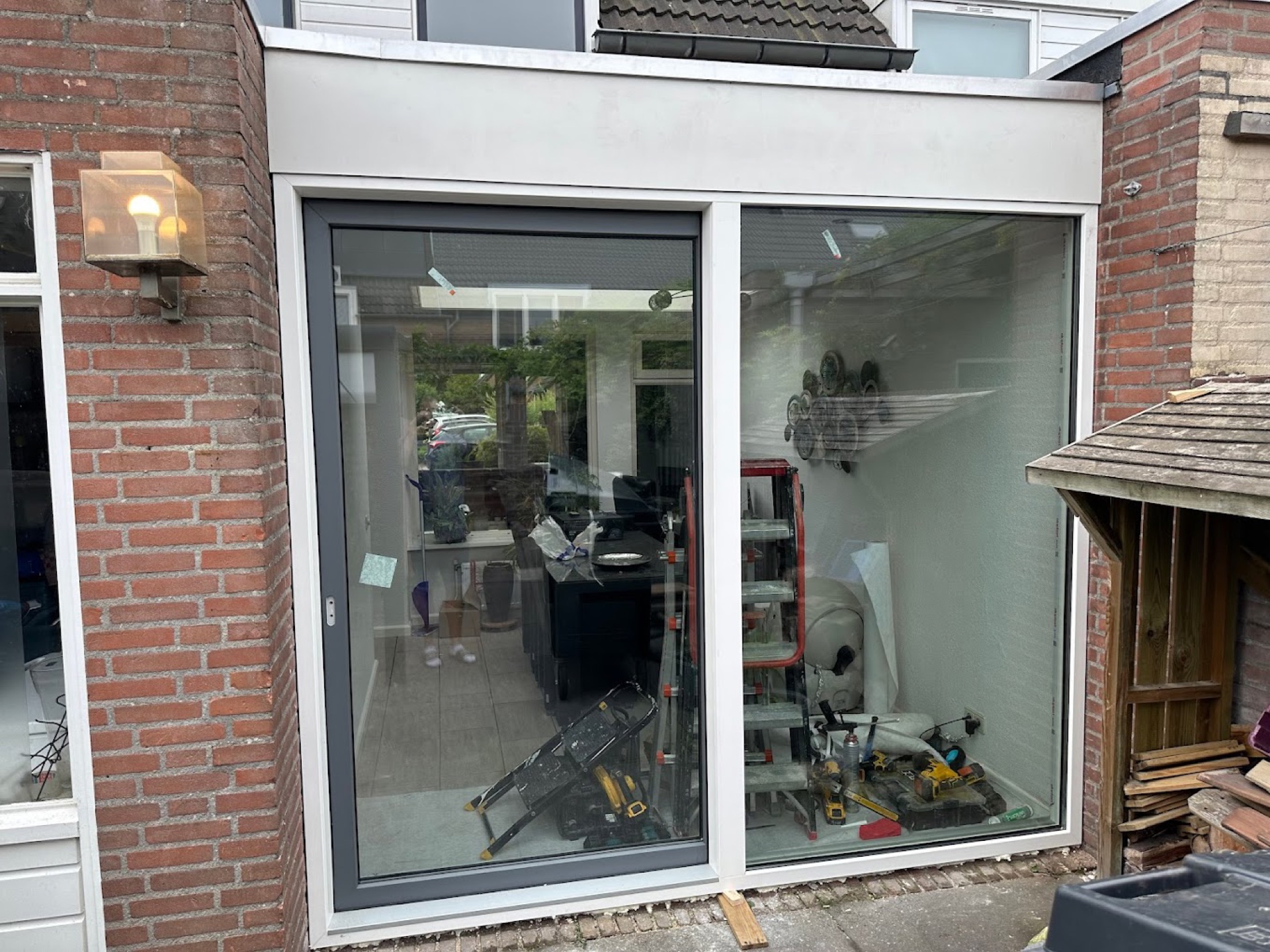 Nieuw geplaatste aluminium schuifpui in een uitbouw, gereedschap en trapladder staan nog binnen
