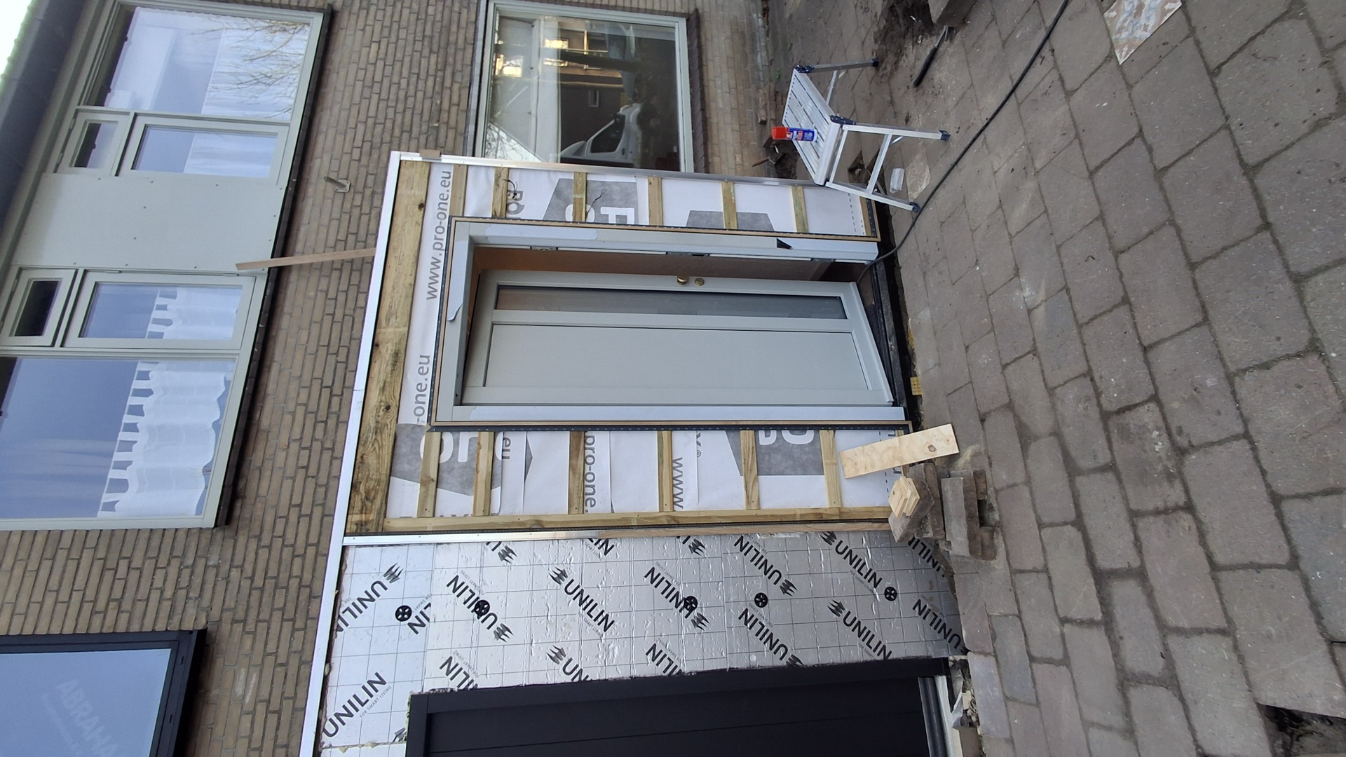 Nieuwe grijze buitendeur gemonteerd in het houten kozijnframe van een aanbouw