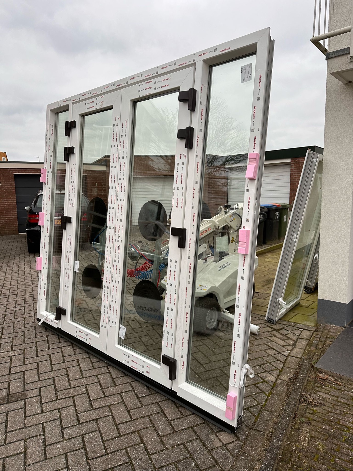 Set nieuwe aluminium deur- en kozijnpanelen met glas, klaargezet op de oprit voor plaatsing