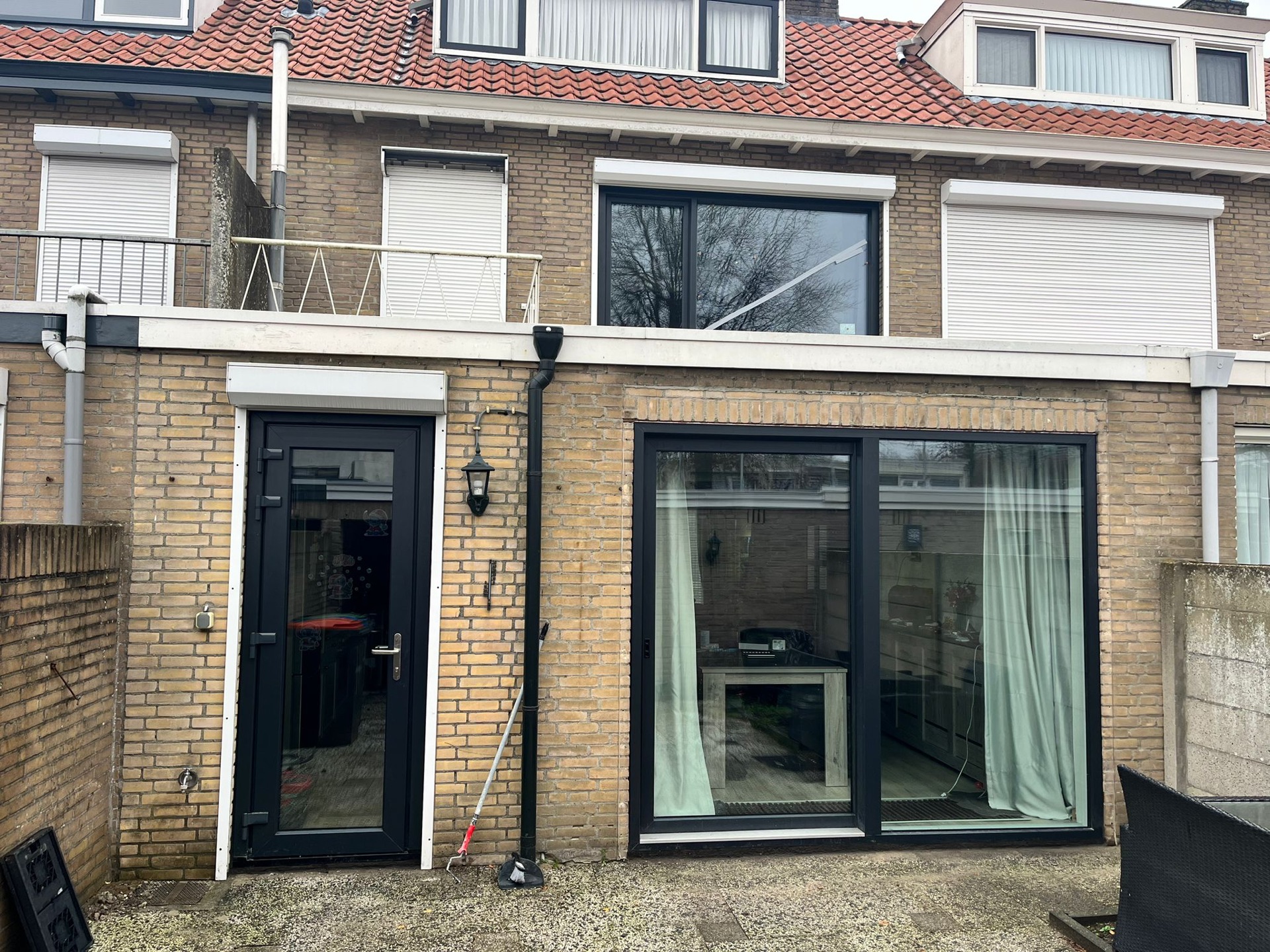 Gevel van een aanbouw met een zwarte openslaande deur en een grote schuifpui