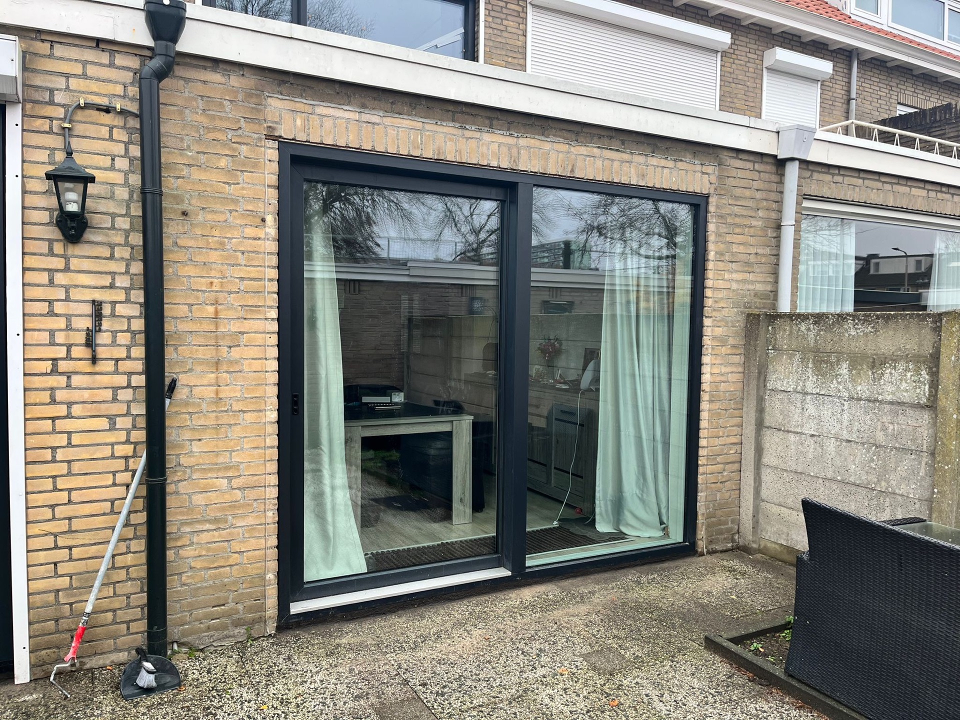 Grote antracietkleurige aluminium schuifpui in een bakstenen aanbouw, gezien vanaf het terras