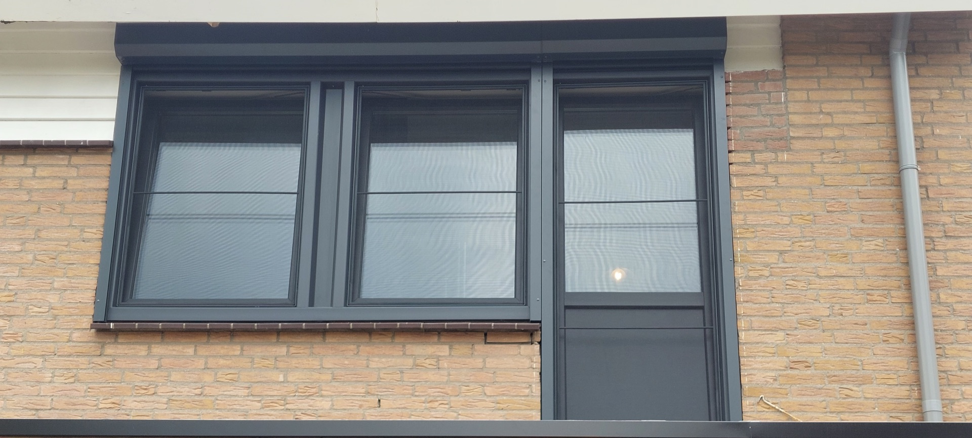 Antracietkleurige aluminium kozijnen met draairaam en deur in een bakstenen gevel