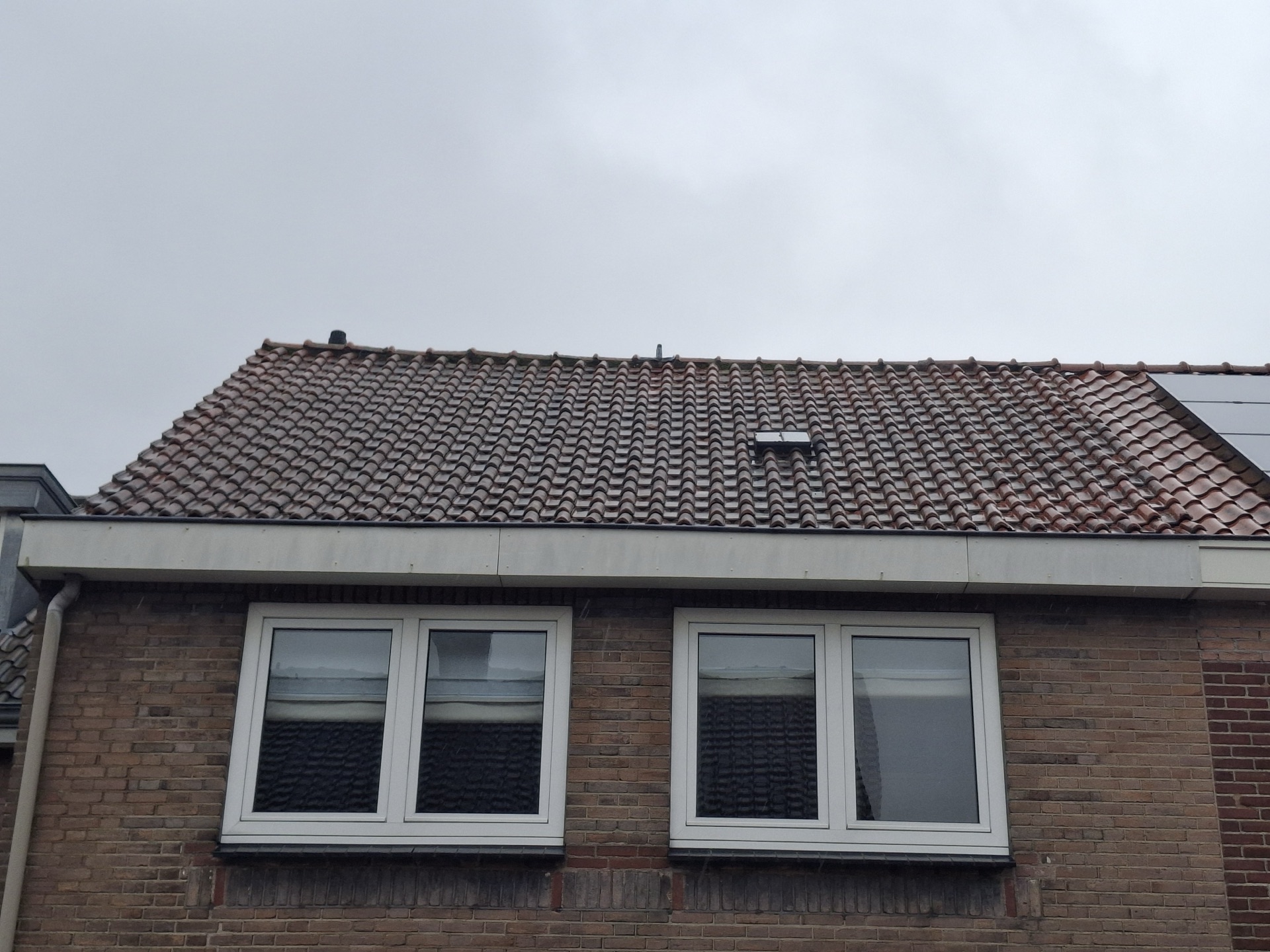 Twee witte kunststof kozijnen onder de dakrand van een woning, met het pannendak erboven