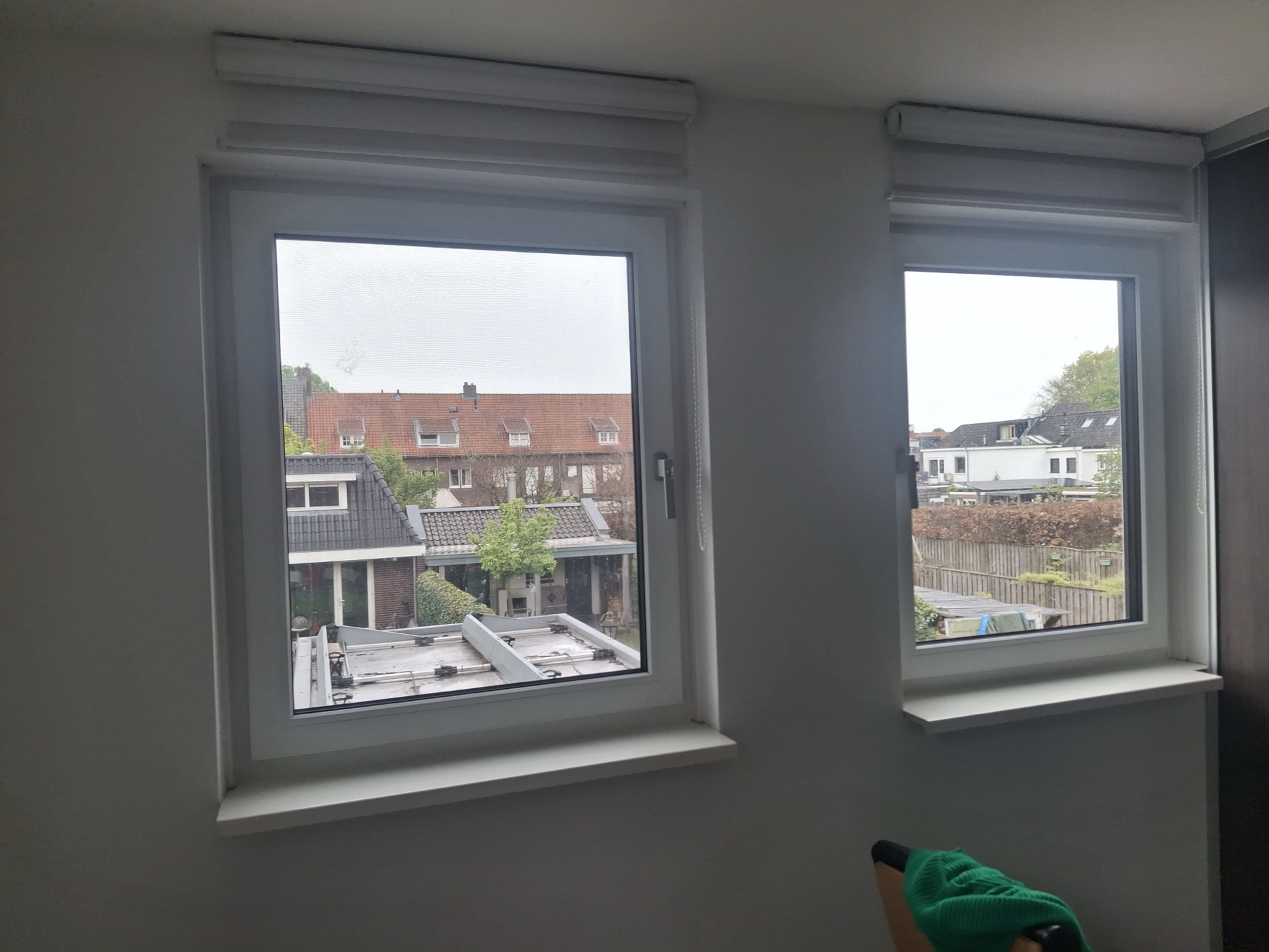Twee nieuwe kunststof kozijnen in een slaapkamer, met uitzicht over de daken van de buurt