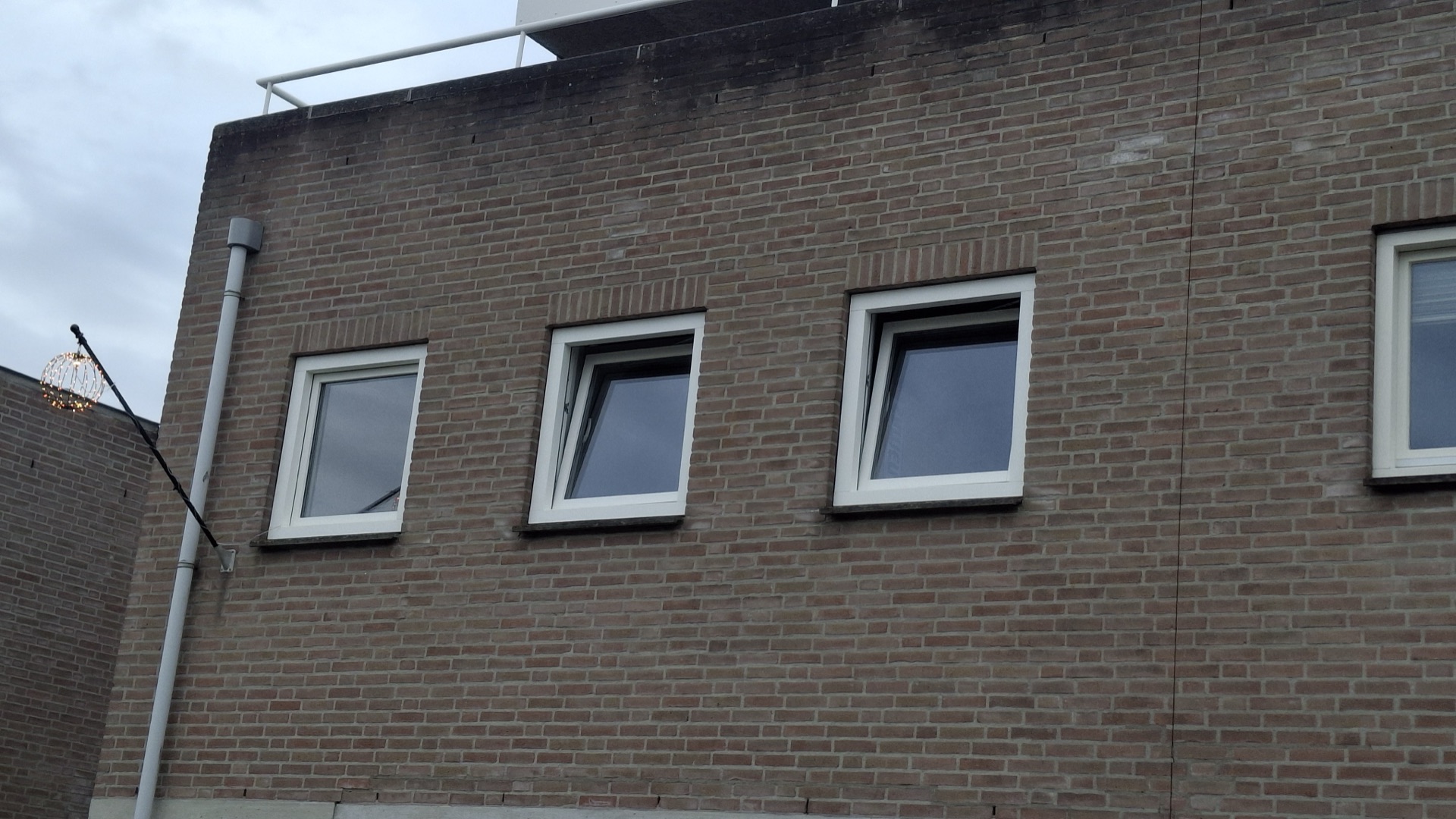 Rij nieuwe witte kunststof kozijnen in een bakstenen gevel, twee ramen staan open