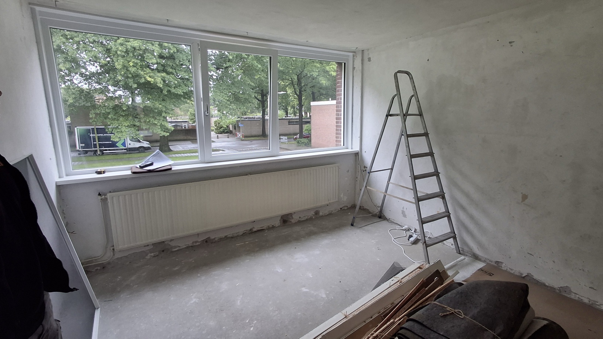 Nieuw kunststof kozijn met drie ramen, geplaatst in een kale renovatieruimte
