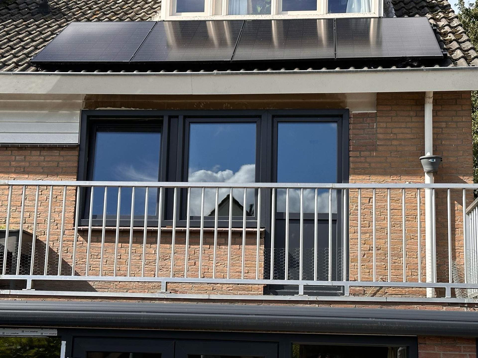 Antracietkleurige aluminium kozijnen op het balkon van een woning met zonnepanelen op het dak
