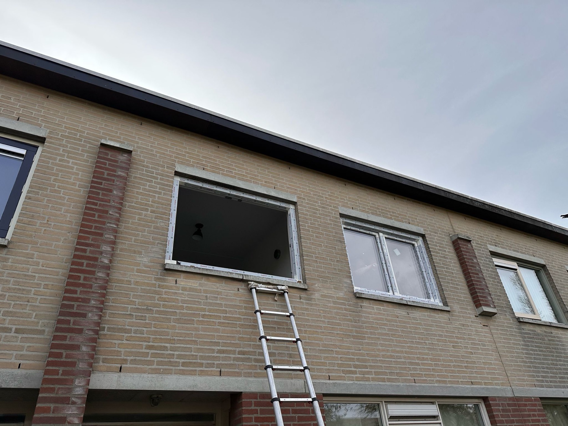 Nieuw kozijn gesteld in de gevelopening, glas nog niet geplaatst, met een ladder ertegenaan