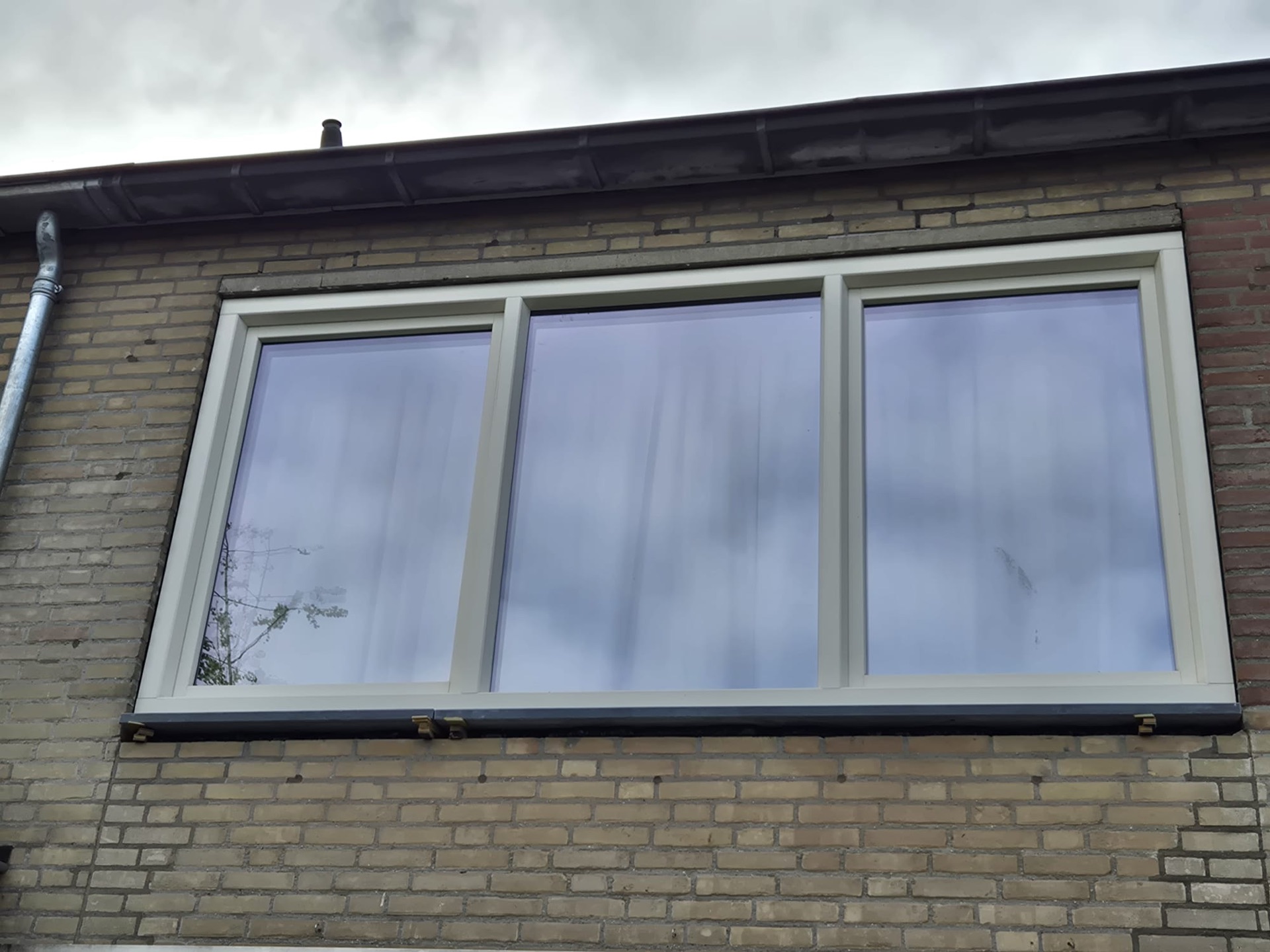Drie witte kunststof kozijnen naast elkaar in een lichte bakstenen gevel
