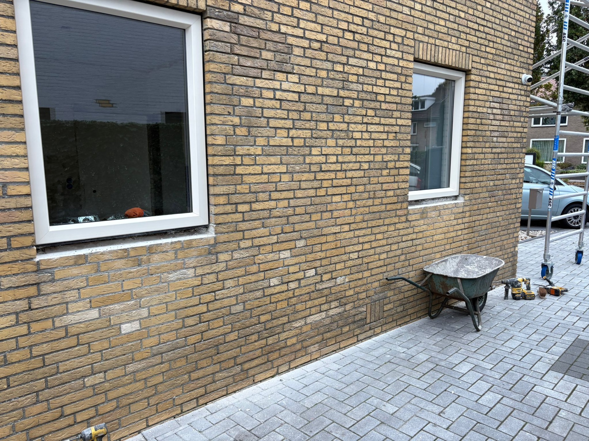 Nieuwe bakstenen gevel van een aanbouw met twee kunststof kozijnen, kruiwagen en gereedschap ervoor