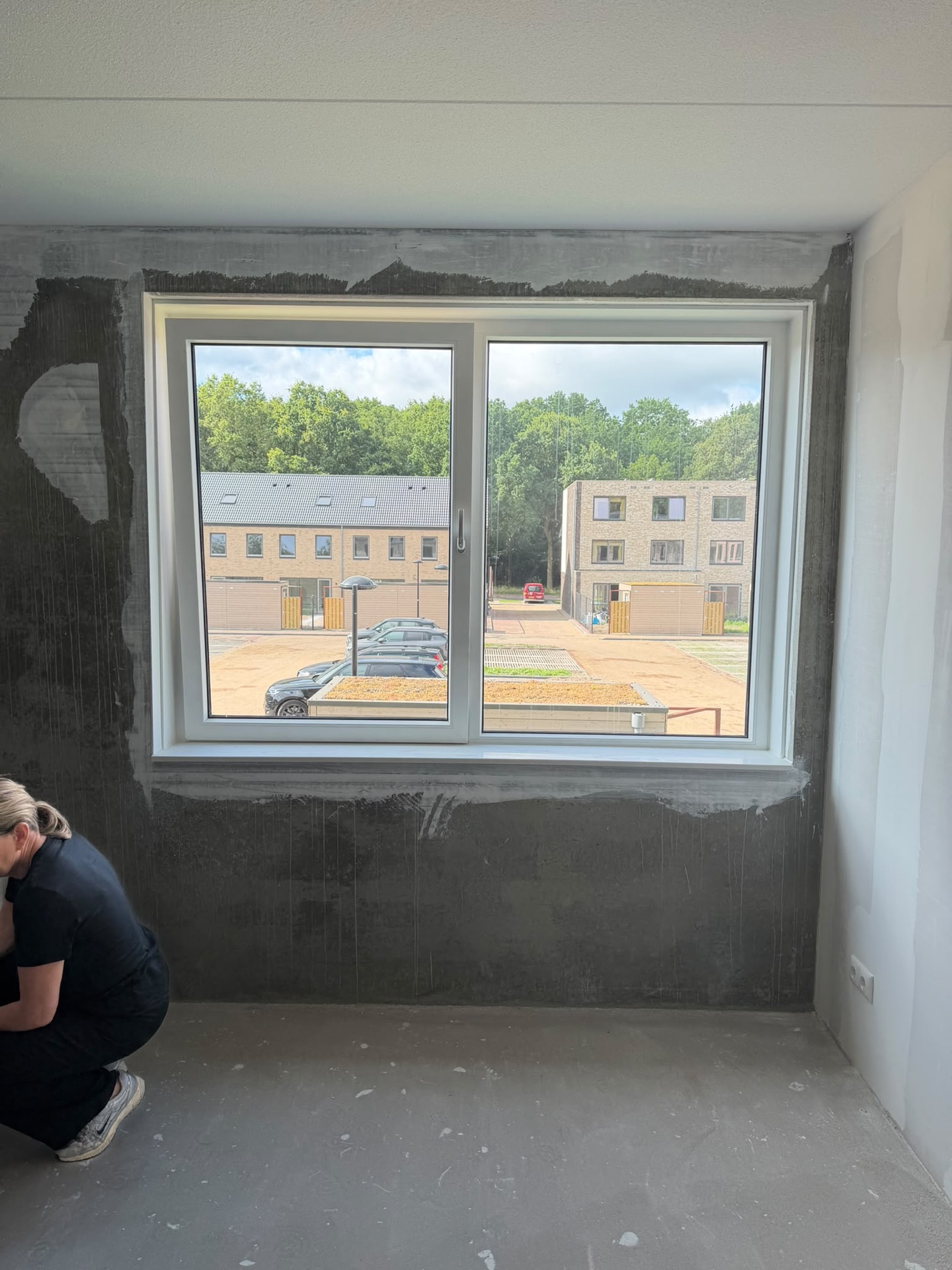 Wit kunststof kozijn met twee raamdelen in een kamer in aanbouw, een medewerker werkt op de vloer