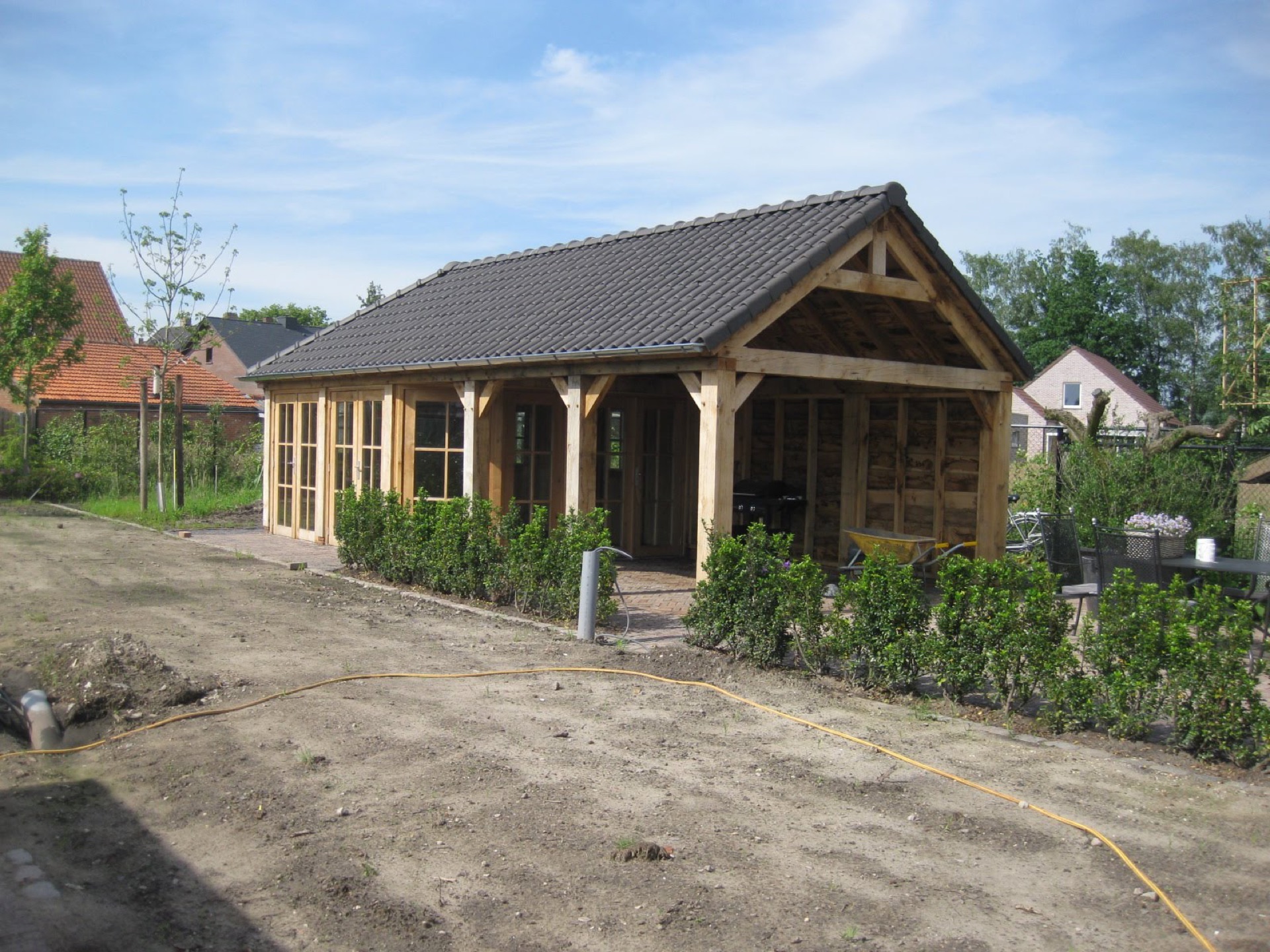 Afgewerkt houten tuinhuis met pannendak en openslaande deuren, de tuin er omheen nog in aanleg