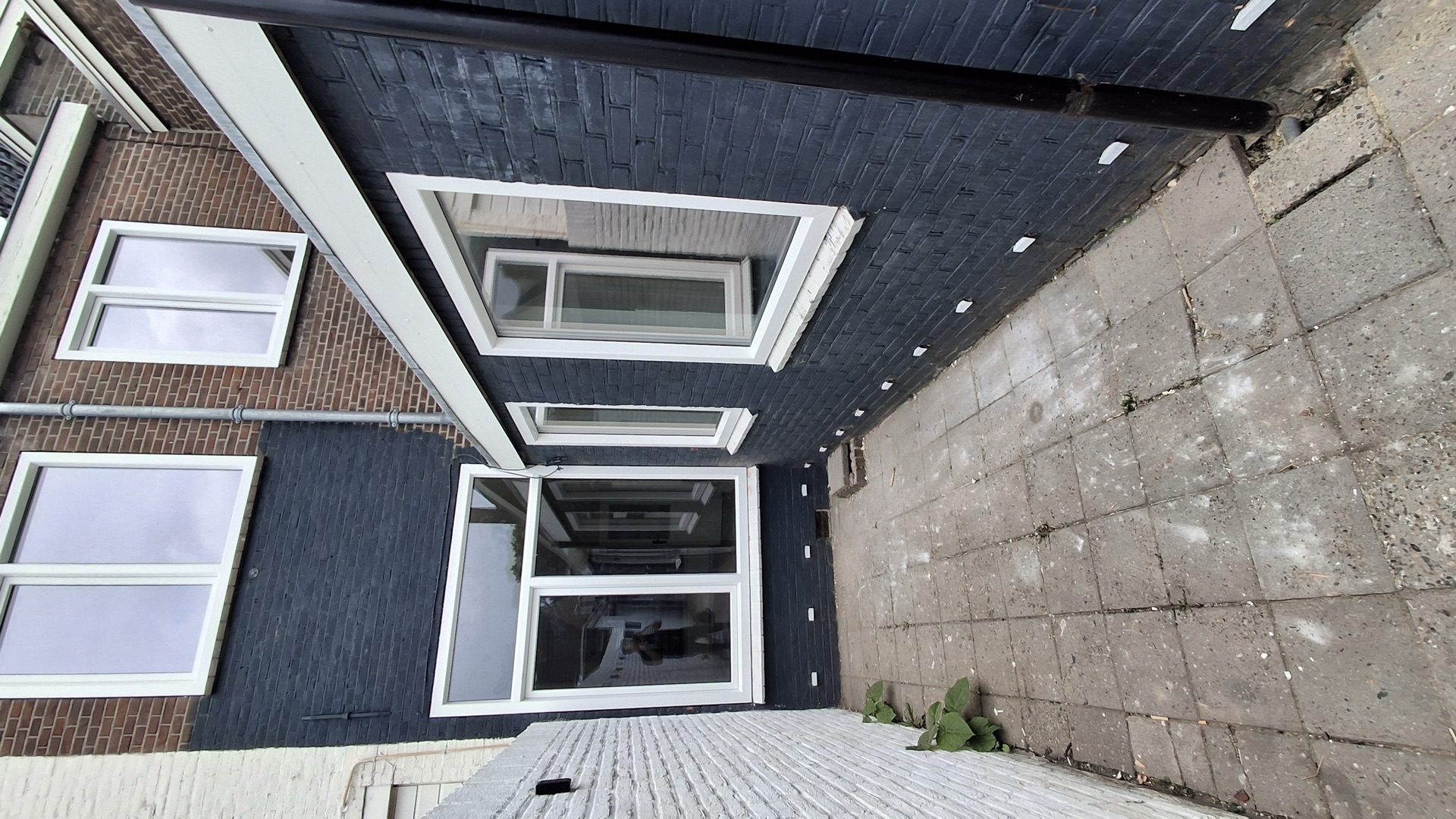 Hoek van een zwart geschilderde bakstenen aanbouw met nieuwe witte kunststof kozijnen aan het terras