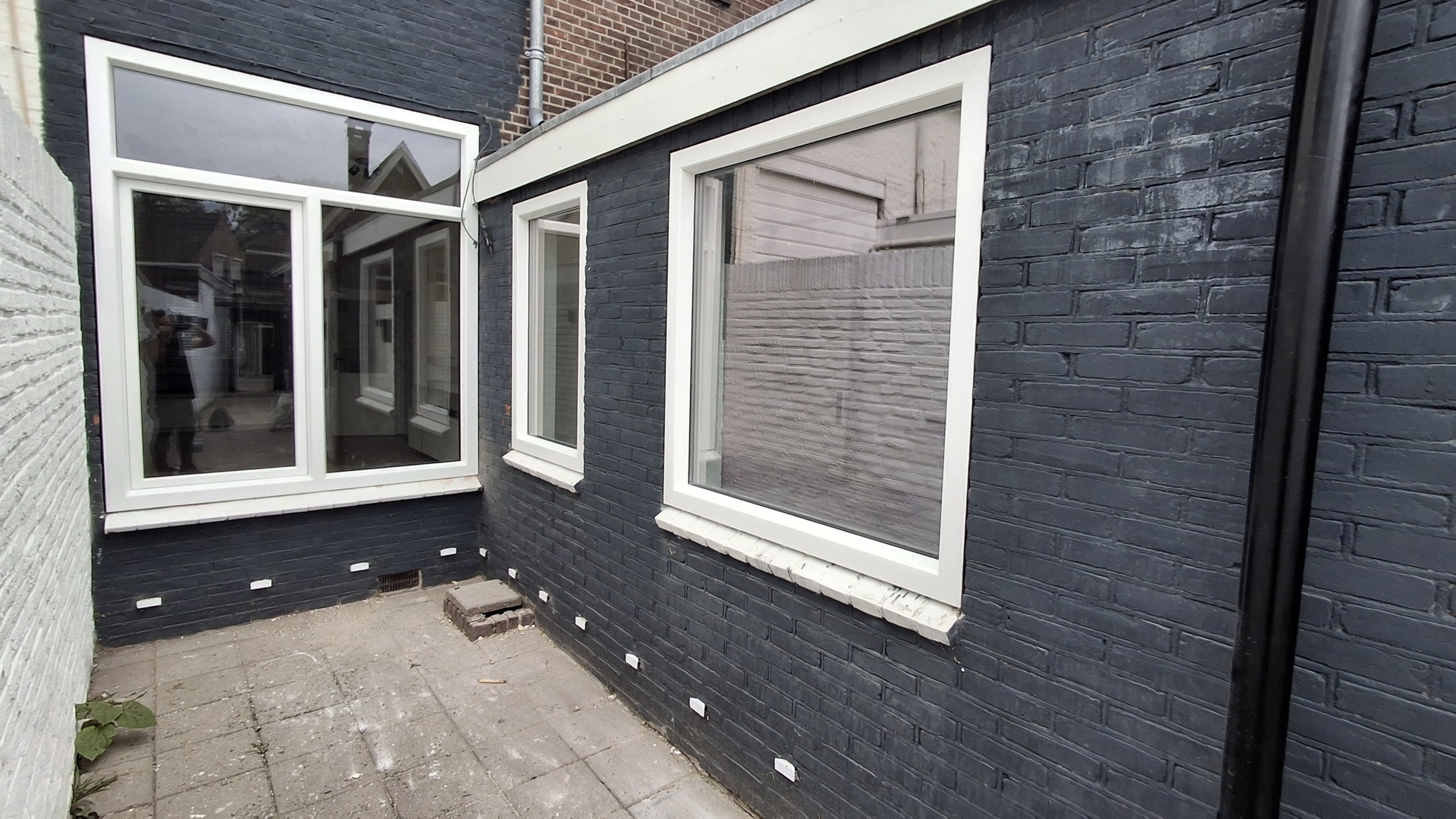 Zwart geschilderde aanbouw met meerdere nieuwe witte kunststof kozijnen