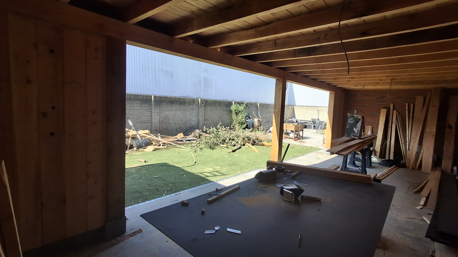 Aanbouw in houtskeletbouw tijdens de opbouw, met werkbank en bouwmateriaal in de tuin