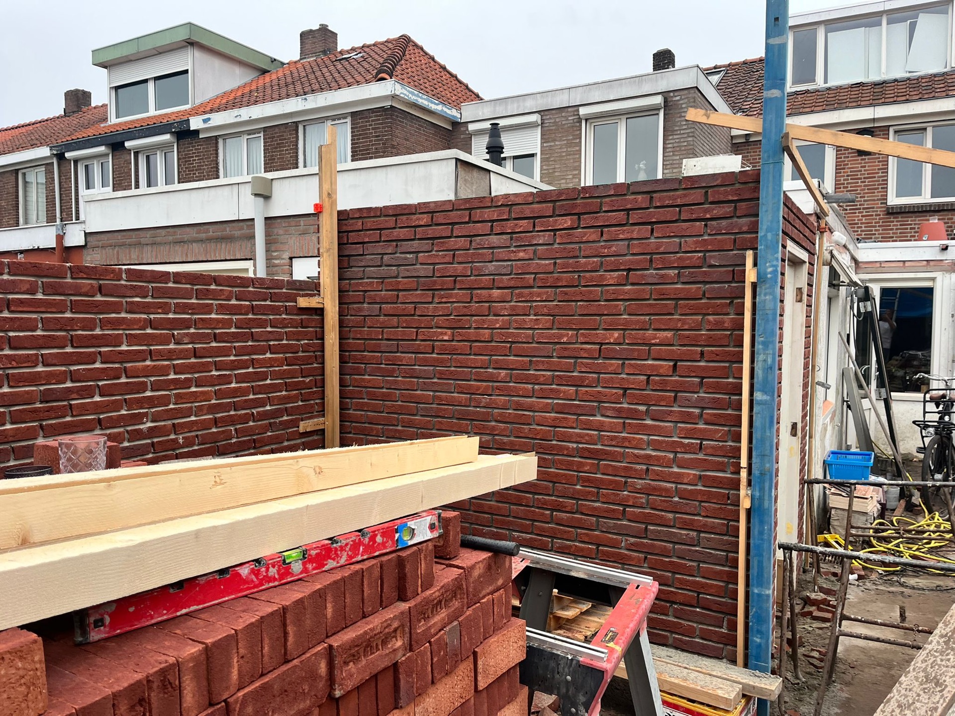 Bakstenen muur van een aanbouw in opbouw, met steigerhout, troffel en waterpas op de bouwplaats